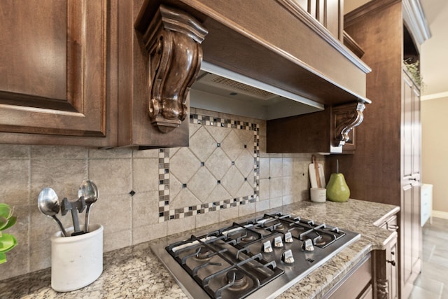 kitchen featuring stainless steel gas cooktop, dark brown cabinets, tasteful backsplash, and light stone countertops