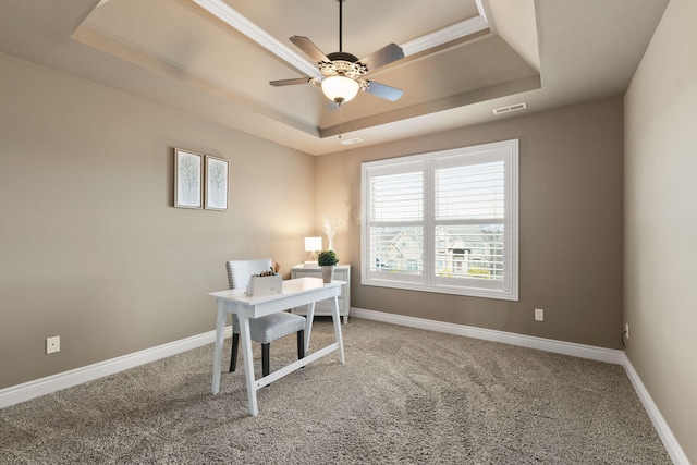 carpeted office space with baseboards, visible vents, a raised ceiling, and a ceiling fan