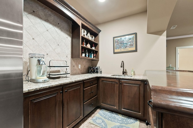 kitchen with light stone counters, decorative backsplash, a sink, dark brown cabinetry, and stainless steel fridge