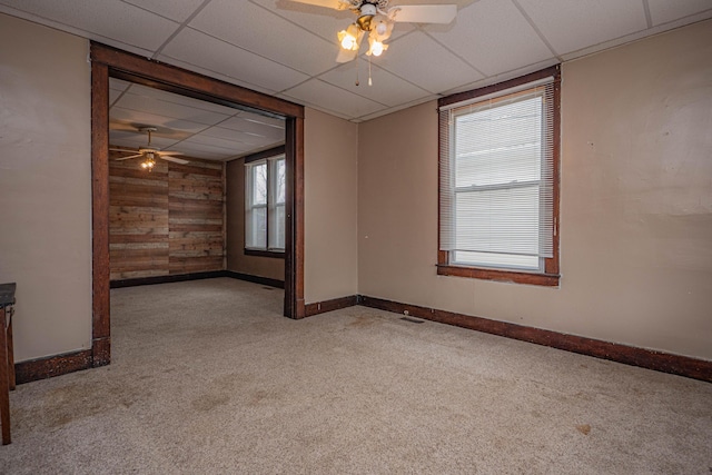 empty room with a paneled ceiling, light carpet, wood walls, and baseboards