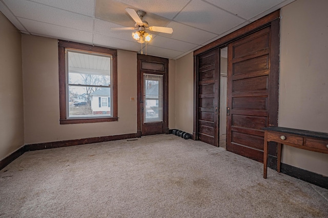 interior space with ceiling fan, baseboards, a drop ceiling, and carpet flooring