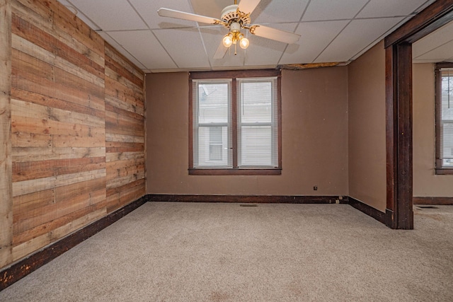 spare room featuring ceiling fan, a paneled ceiling, carpet floors, wood walls, and baseboards