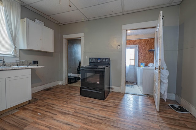 kitchen featuring light countertops, washing machine and dryer, white cabinetry, and black / electric stove