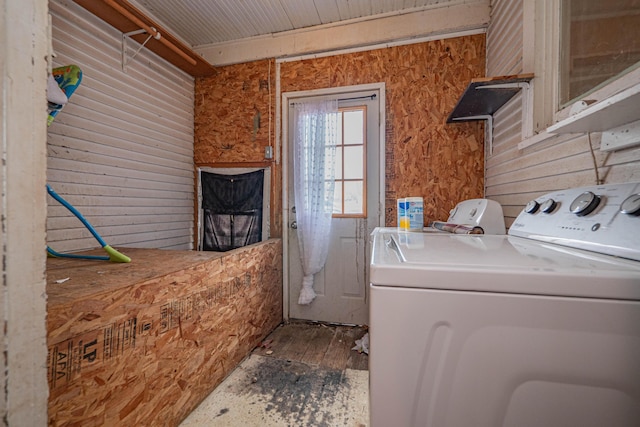 clothes washing area featuring laundry area, wooden walls, and washer and clothes dryer