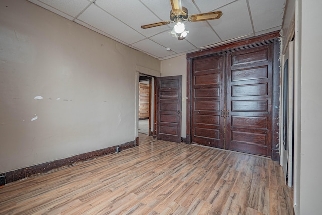 unfurnished bedroom featuring ceiling fan, baseboards, a drop ceiling, and wood finished floors