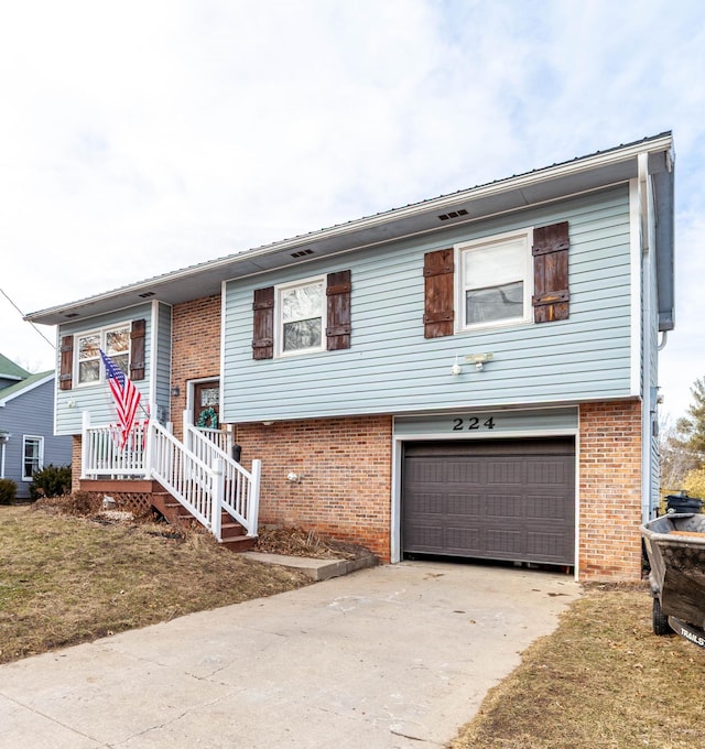 raised ranch featuring a garage, a front yard, concrete driveway, and brick siding