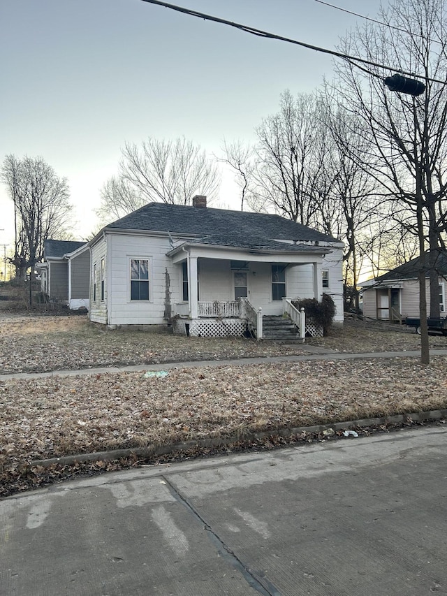 bungalow-style home featuring covered porch, a chimney, and roof with shingles