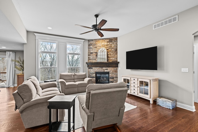 living area with ceiling fan, a fireplace, visible vents, and dark wood finished floors