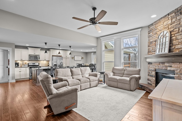 living area with a ceiling fan, recessed lighting, dark wood-style flooring, and a stone fireplace