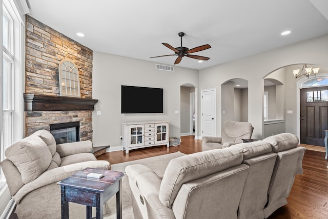 living room with a stone fireplace, recessed lighting, ceiling fan with notable chandelier, dark wood-type flooring, and visible vents