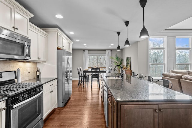 kitchen with appliances with stainless steel finishes, dark wood-type flooring, decorative light fixtures, white cabinetry, and a sink