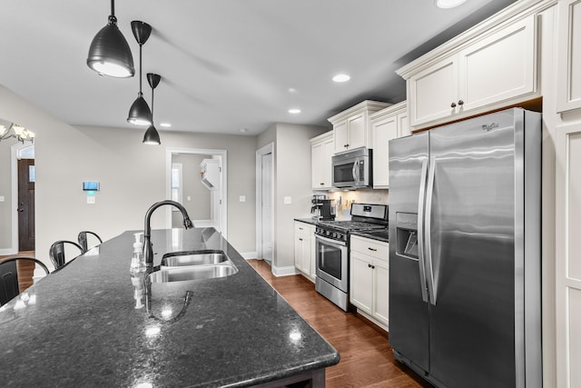 kitchen with stainless steel appliances, a sink, hanging light fixtures, dark wood-style floors, and dark stone countertops