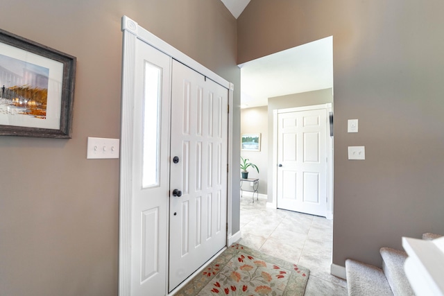 foyer entrance featuring light tile patterned flooring, baseboards, and stairs