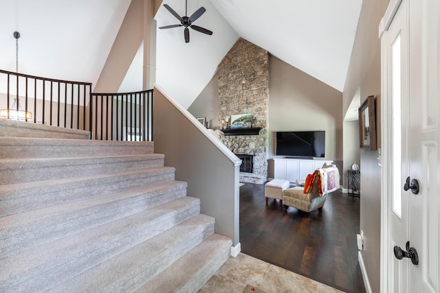 stairs featuring a fireplace, a ceiling fan, wood finished floors, high vaulted ceiling, and baseboards