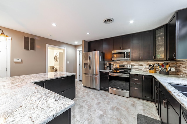 kitchen with appliances with stainless steel finishes, stacked washer / drying machine, visible vents, and backsplash