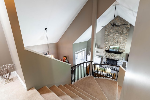 stairs with carpet floors, a fireplace, a ceiling fan, high vaulted ceiling, and baseboards