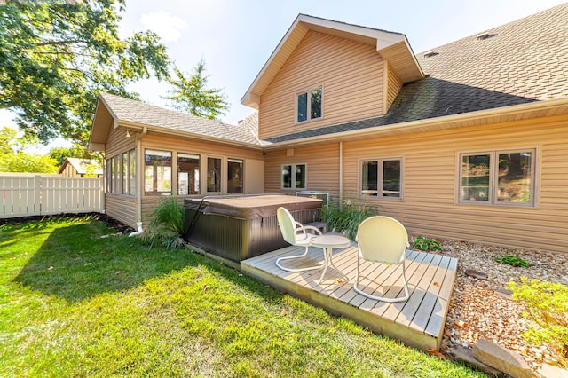 rear view of house with a yard, a shingled roof, a hot tub, a sunroom, and fence