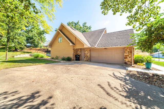 view of front of home with a garage, a shingled roof, concrete driveway, stone siding, and a front yard