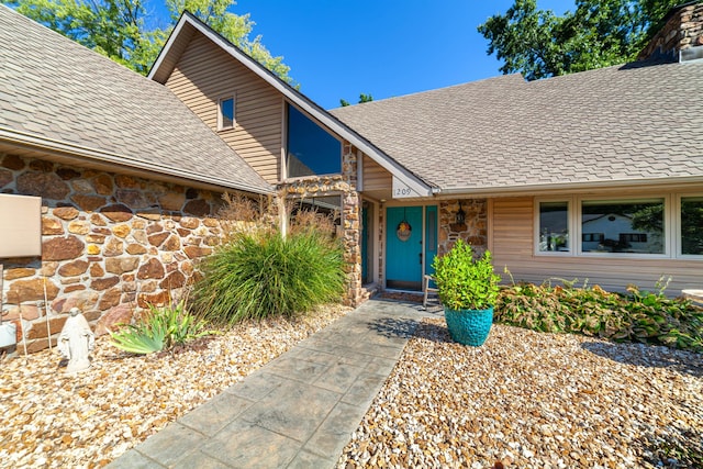 entrance to property with stone siding and a shingled roof