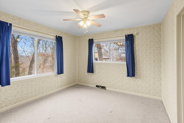 empty room with wallpapered walls, visible vents, baseboards, a ceiling fan, and carpet