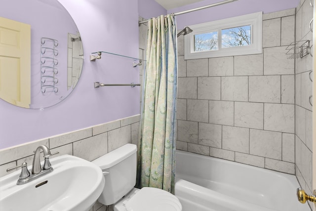 bathroom with wainscoting, toilet, a sink, shower / bath combination with curtain, and tile walls