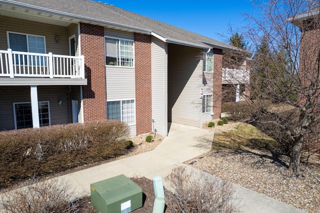 exterior space featuring a balcony, brick siding, and a shingled roof