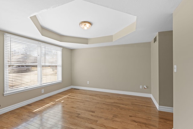 empty room with baseboards, visible vents, a tray ceiling, and hardwood / wood-style floors