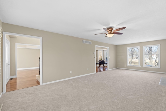 spare room with light carpet, ceiling fan, visible vents, and baseboards