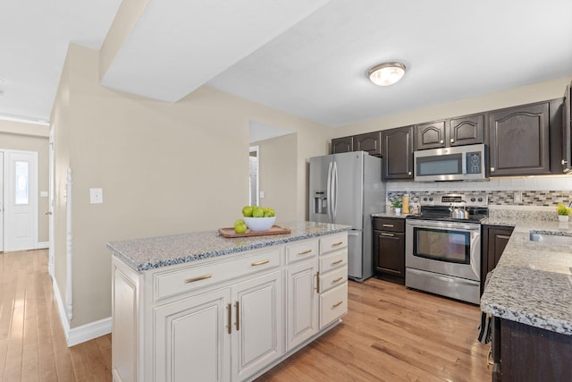 kitchen featuring appliances with stainless steel finishes, a center island, light wood-style flooring, and decorative backsplash