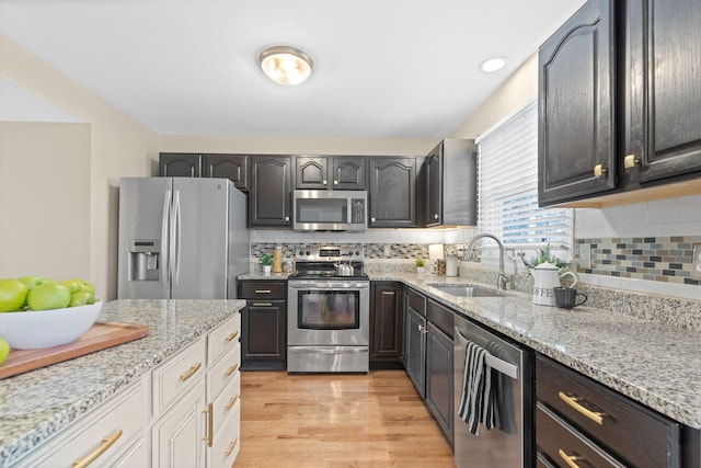 kitchen featuring stainless steel appliances, light wood finished floors, backsplash, and a sink