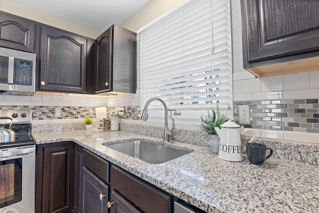 kitchen featuring dark brown cabinetry, light stone counters, a sink, stainless steel appliances, and backsplash