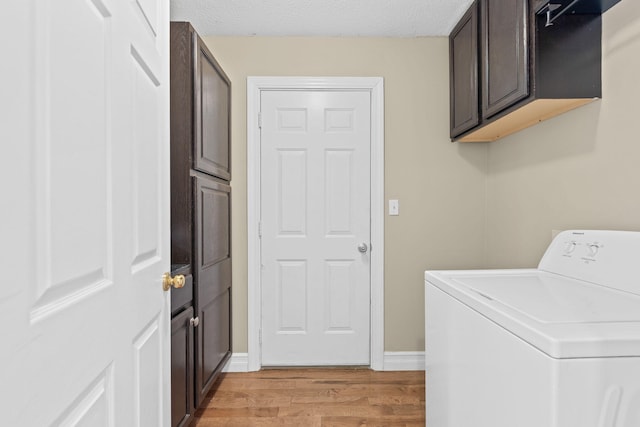 washroom featuring a textured ceiling, baseboards, light wood-type flooring, cabinet space, and washer / dryer