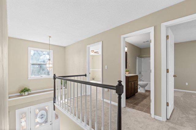 hallway with light carpet, a textured ceiling, an upstairs landing, and baseboards