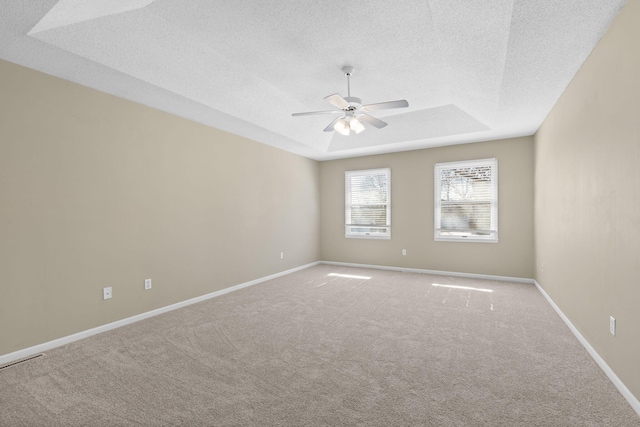 carpeted empty room featuring a ceiling fan, a tray ceiling, a textured ceiling, and baseboards