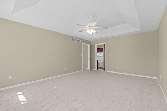 carpeted spare room featuring ceiling fan, a tray ceiling, visible vents, and baseboards