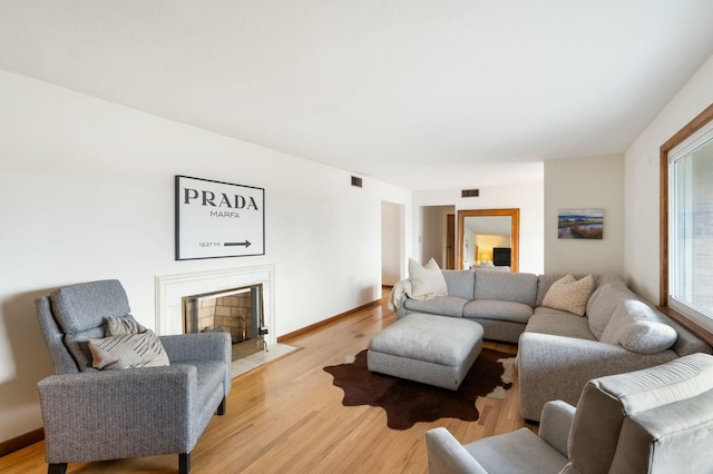 living room featuring visible vents, a fireplace with flush hearth, light wood-style flooring, and baseboards