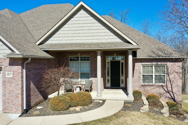 view of front of home with covered porch, roof with shingles, and brick siding