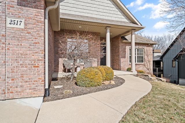 doorway to property with brick siding and roof with shingles