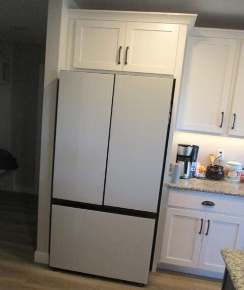 kitchen featuring light stone counters, light wood-style floors, freestanding refrigerator, and white cabinets