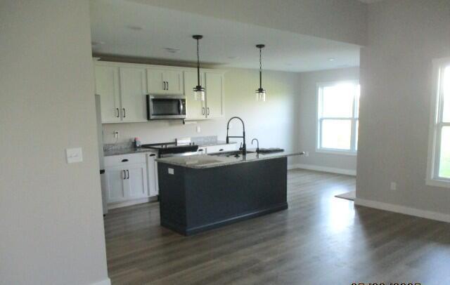 305 E Francis St, Sturgeon, MO 65284 - kitchen featuring stainless steel microwave, baseboards, dark wood finished floors, white cabinets, and a kitchen island with sink