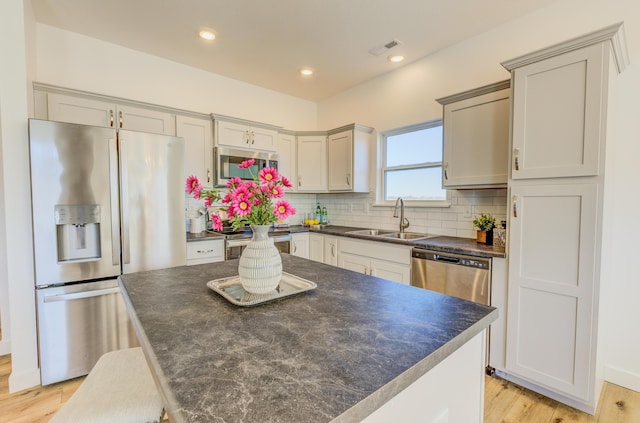 kitchen featuring stainless steel appliances, a sink, visible vents, backsplash, and dark countertops