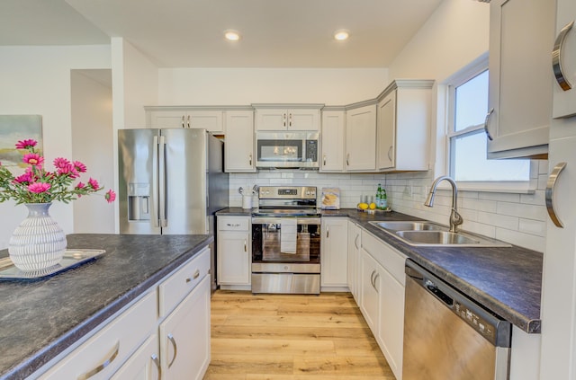 kitchen with dark countertops, a sink, stainless steel appliances, light wood-type flooring, and backsplash