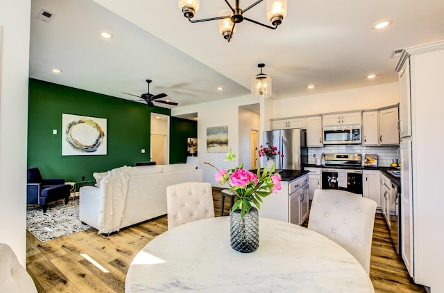 dining area with ceiling fan with notable chandelier, light wood-style flooring, and recessed lighting