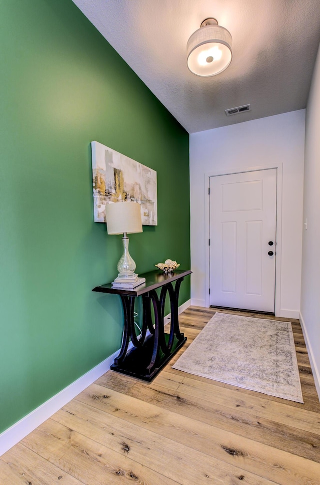 foyer entrance with visible vents, baseboards, and wood finished floors