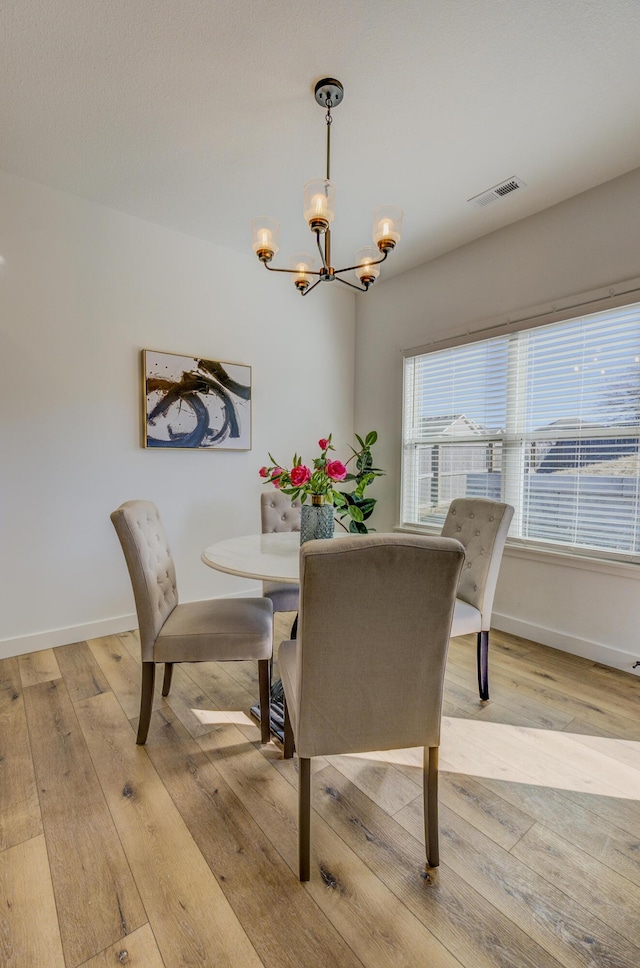 dining space featuring light wood finished floors, baseboards, visible vents, and a chandelier