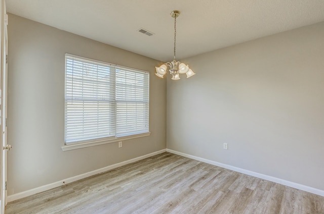 empty room featuring light wood finished floors, baseboards, visible vents, and a notable chandelier