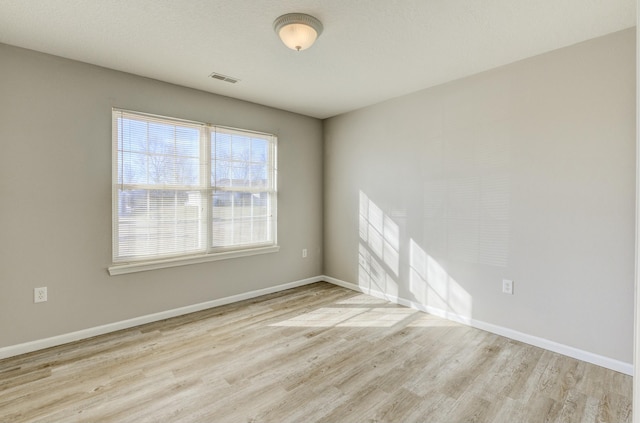 unfurnished room featuring light wood-type flooring, visible vents, and baseboards