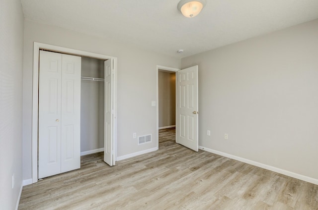 unfurnished bedroom featuring light wood finished floors, baseboards, visible vents, and a closet