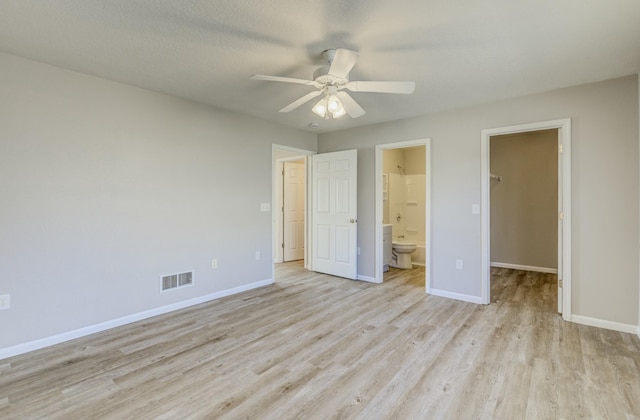 unfurnished bedroom featuring a walk in closet, light wood finished floors, a closet, visible vents, and baseboards