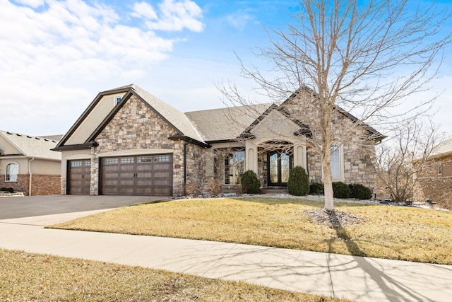 french country home with french doors, a garage, stone siding, driveway, and a front lawn